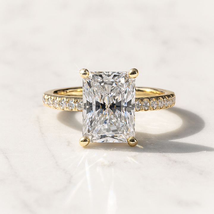Radiant cut diamond engagement ring in yellow gold with pavé diamond band on marble background – Shapiro Diamonds Dallas